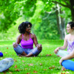 A group of women sit in a circle at an outdoor fitness class in summer